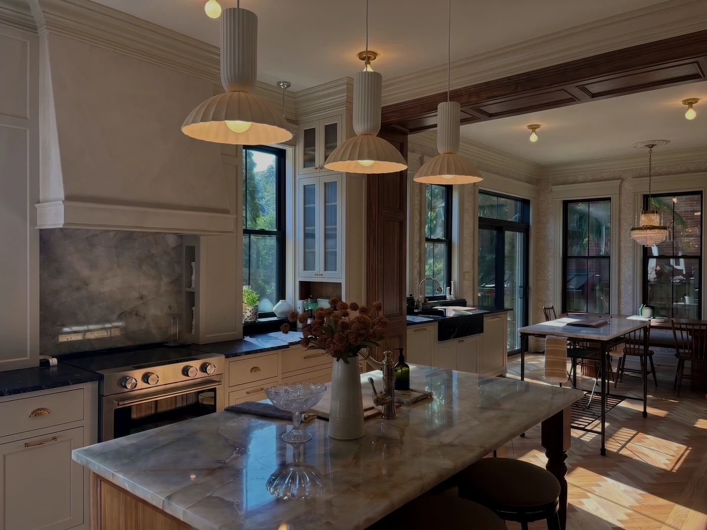 Timeless kitchen with stone island, custom millwork, sculptural pendant lighting, and adjoining dining area